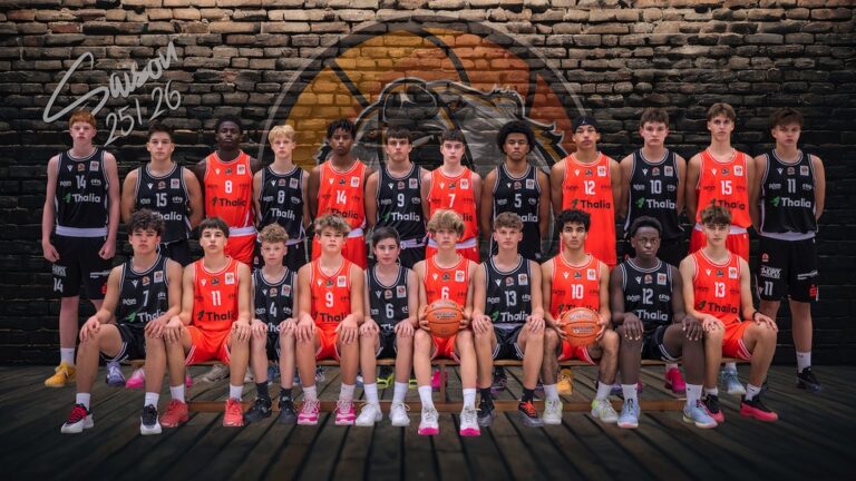 Eine Basketball Jugendmannschaft in schwarzen und orangefarbenen Trikots posiert ernst