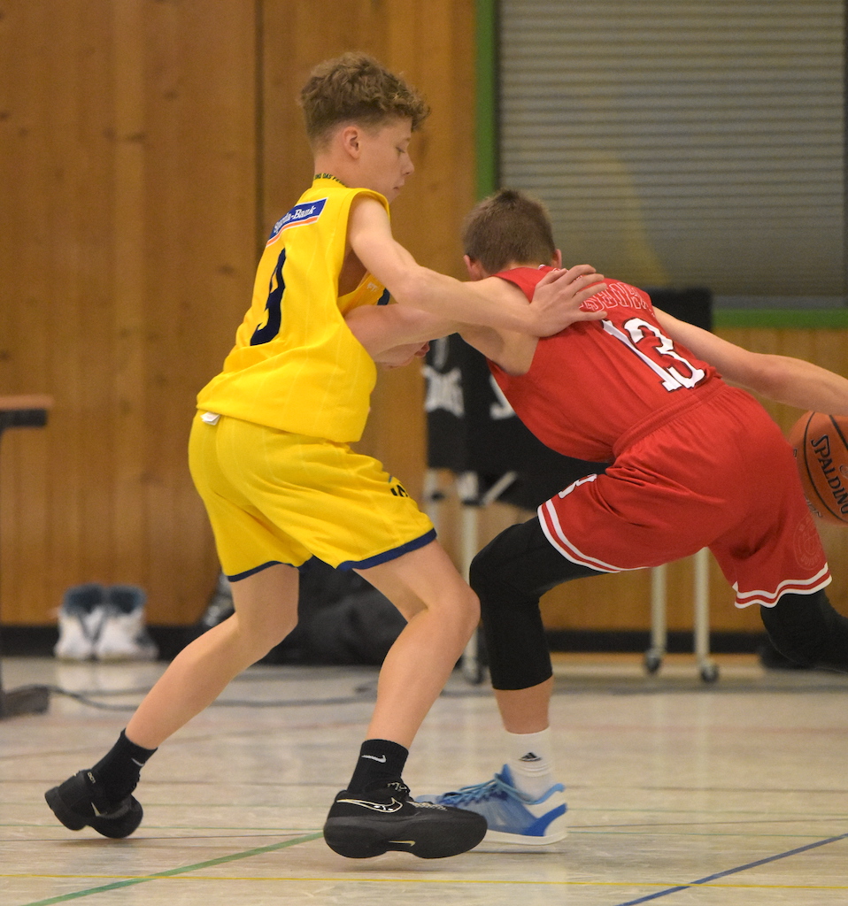 Ein junger Spieler in einem gelben Trikot verteidigt gegen einen in Rot gekleideten Spieler.