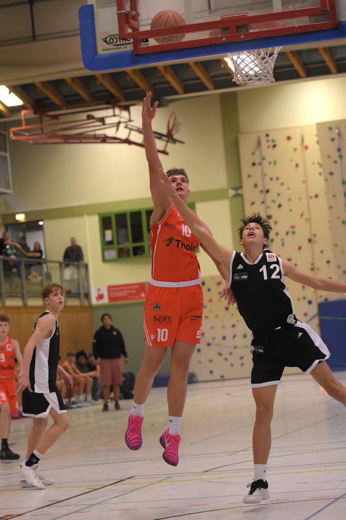 Ein junger Basketballspieler im orangefarbenen Trikot springt zum Korb und wirkt entschlossen