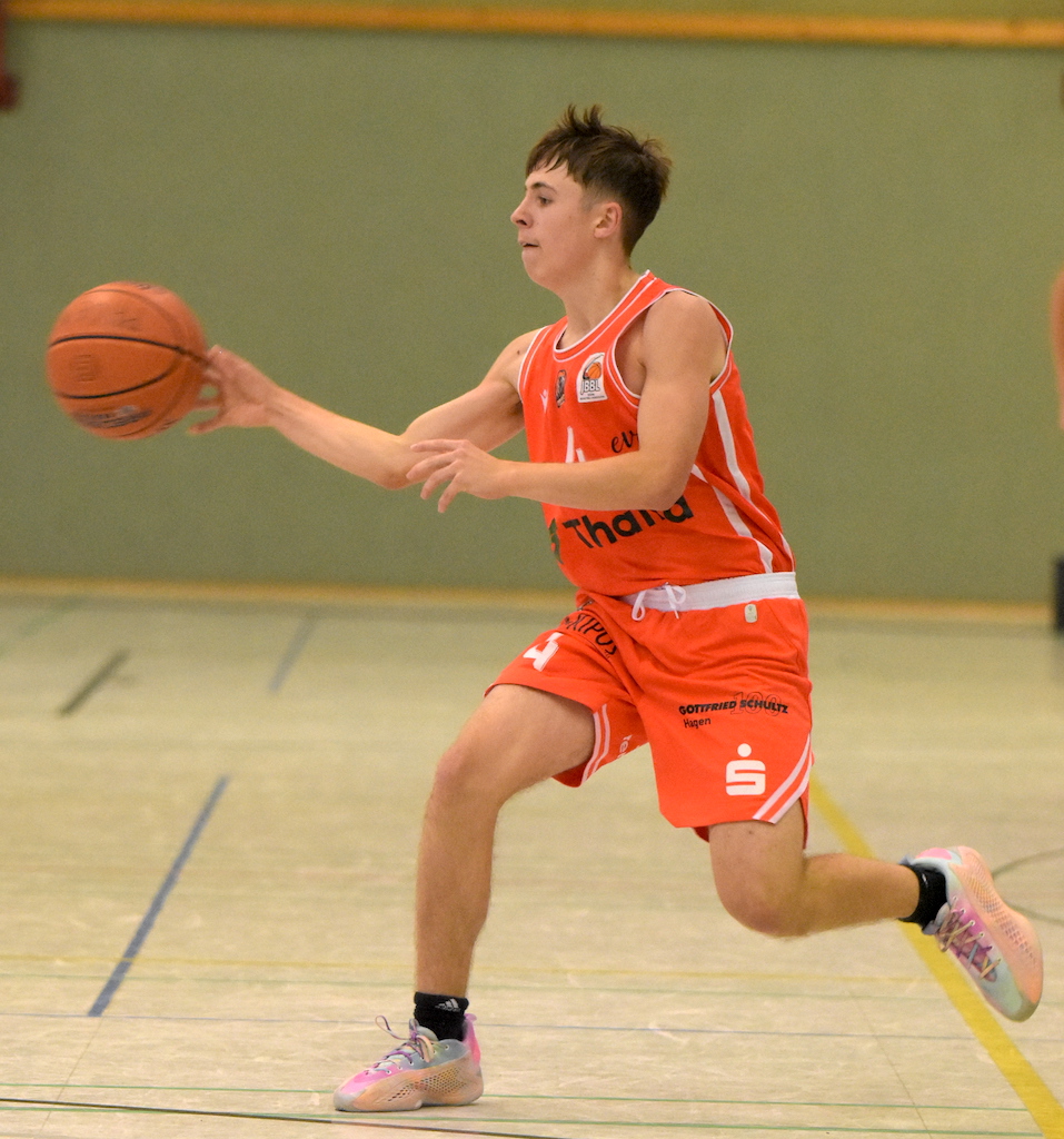 Ein junger Mann im orangefarbenen Basketballtrikot passt konzentriert den Ball