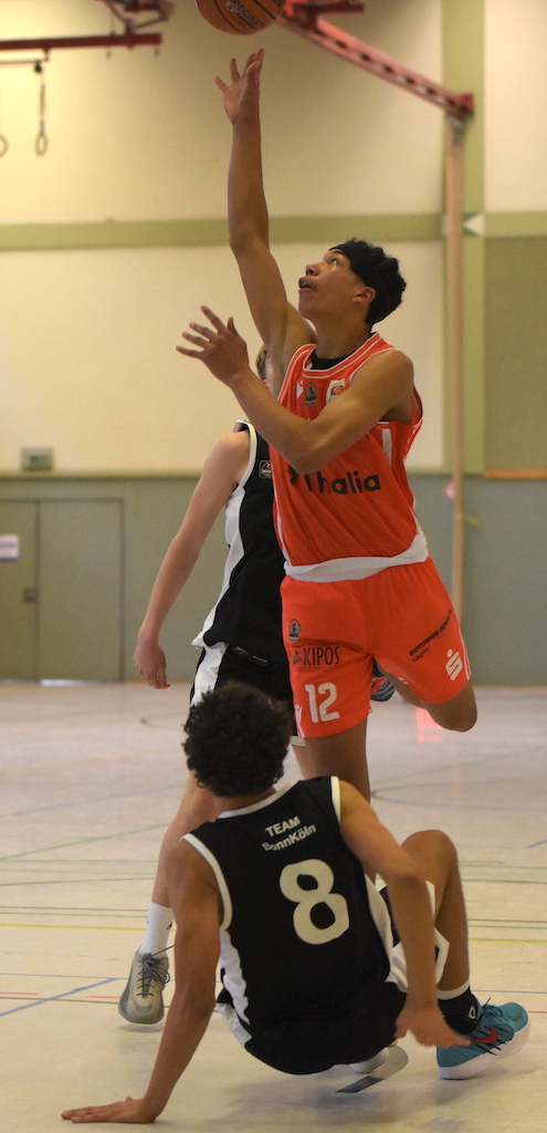 Ein junger Basketballspieler im roten Trikot springt lächelnd zum Korb hoch
