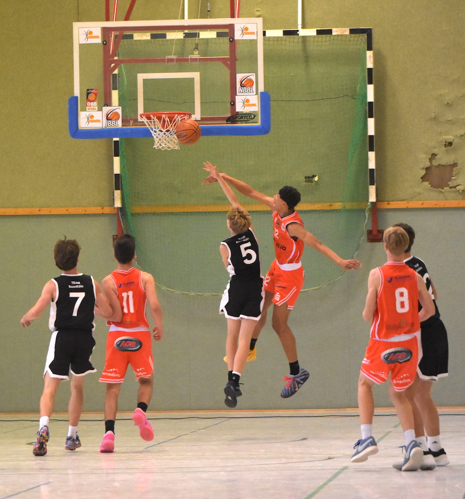 Jugendliche Basketballspieler in Schwarz und Orange springen dynamisch beim Korbleger