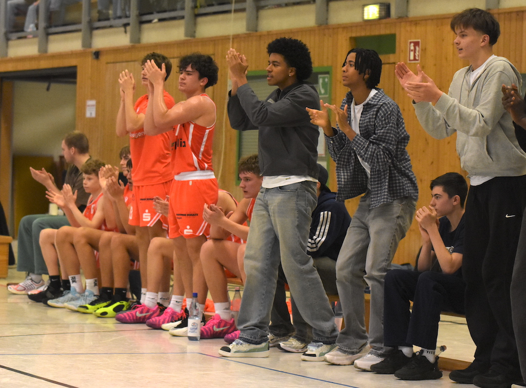 Junge Basketballspieler jubeln lächelnd und applaudierend in einer Sporthalle