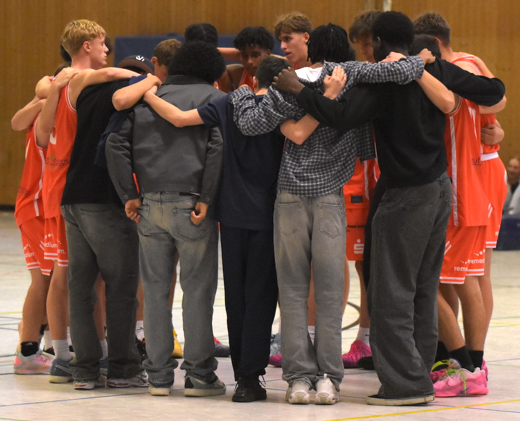 Eine Basketballmannschaft in roten Trikots umarmt sich vor dem Spiel im Kreis