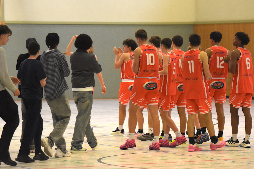 Eine Basketballmannschaft in orangefarbenen Trikots applaudiert jubelnd in der Halle