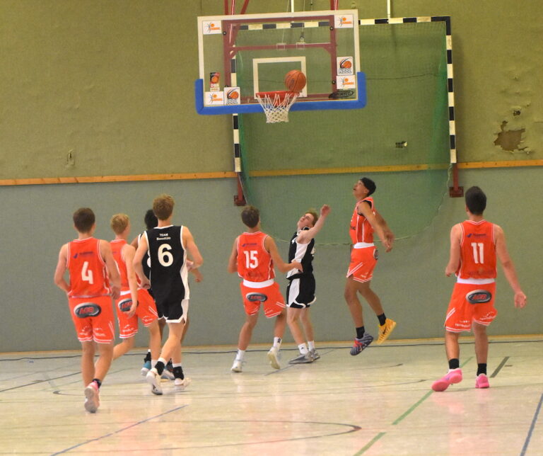 Sechs junge Basketballspieler in roten und schwarzen Trikots beim Korbwurf