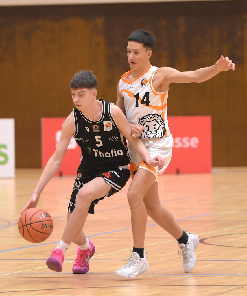 Zwei junge Basketballspieler im Spiel, konzentriert, einer im schwarzen und einer im weißen Trikot