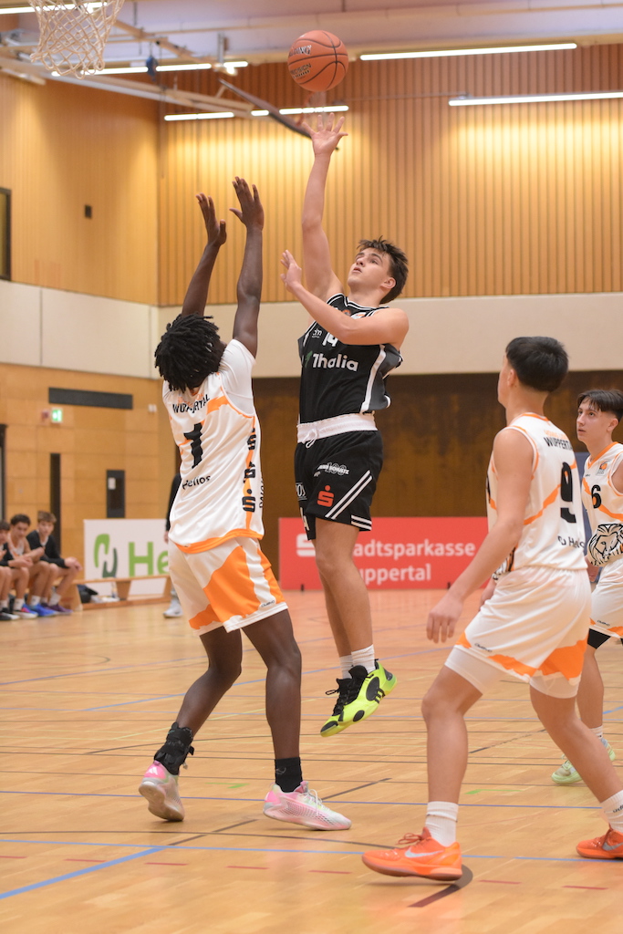 Ein junger Basketballspieler in Schwarz springt zum Korb, während ein Gegenspieler in Weiß versucht, den Wurf zu blocken
