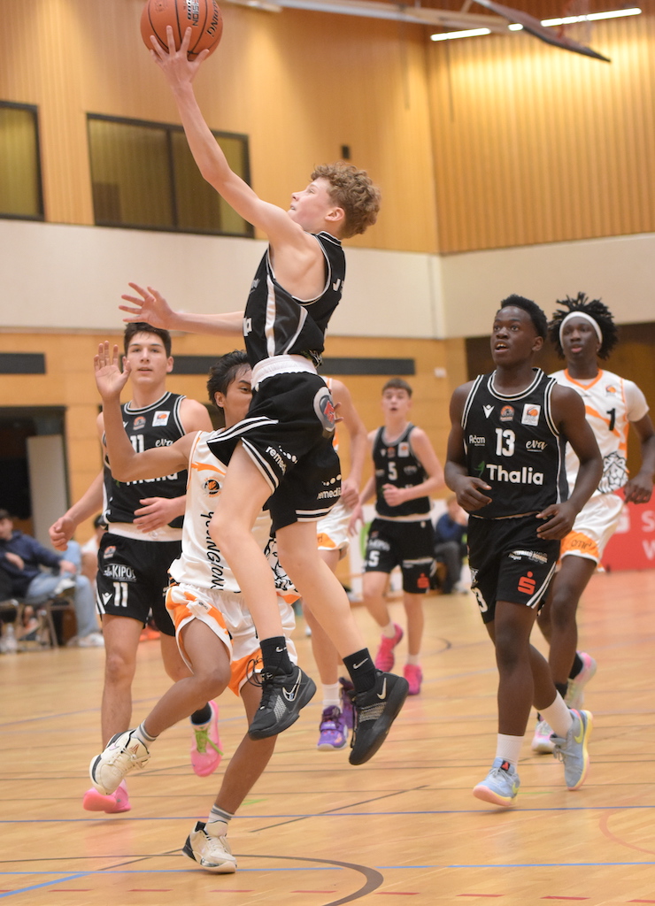 Ein junger Basketballspieler in Schwarz springt dynamisch zum Korb und wirkt konzentriert