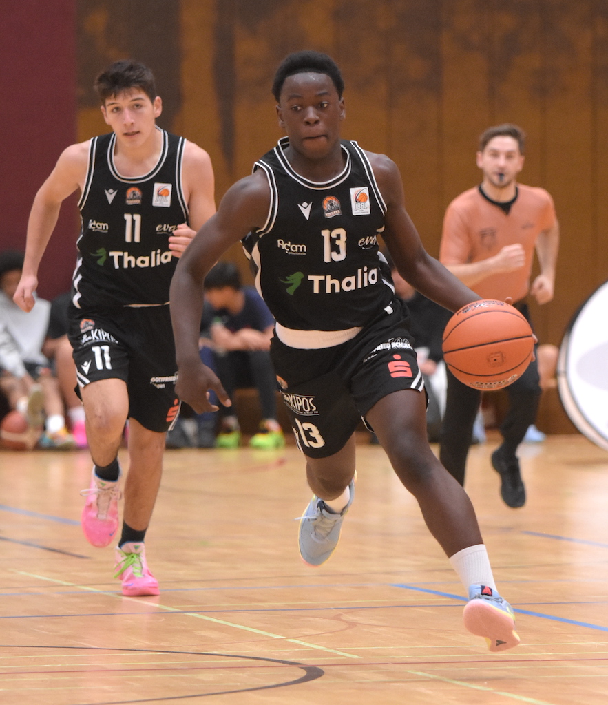 Ein konzentrierter junger Basketballspieler im schwarzen Trikot dribbelt den Ball schnell