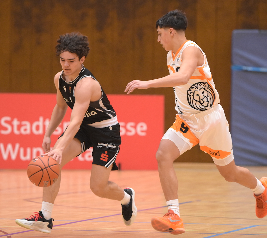 Zwei junge Basketballspieler im Spiel, einer im schwarzen und einer im weißen Trikot