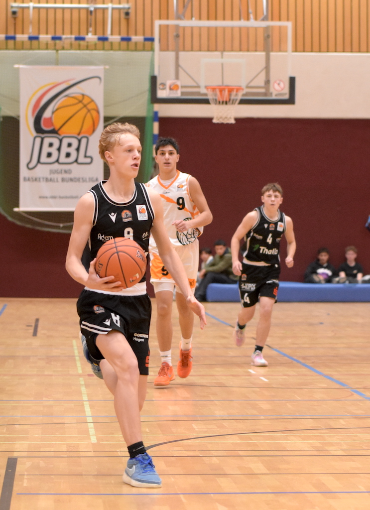 Ein junger Basketballspieler im schwarzen Trikot mit konzentriertem Blick dribbelt den Ball
