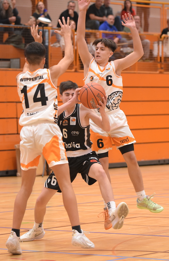 Drei junge Basketballspieler im Spiel, einer hält den Ball, zwei verteidigen aktiv