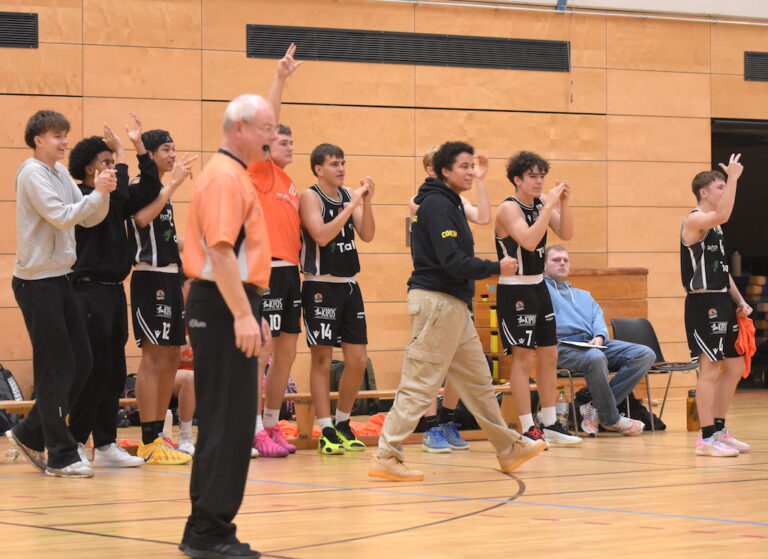 Mehrere junge Basketballspieler jubeln am Spielfeldrand, ein Trainer steht daneben