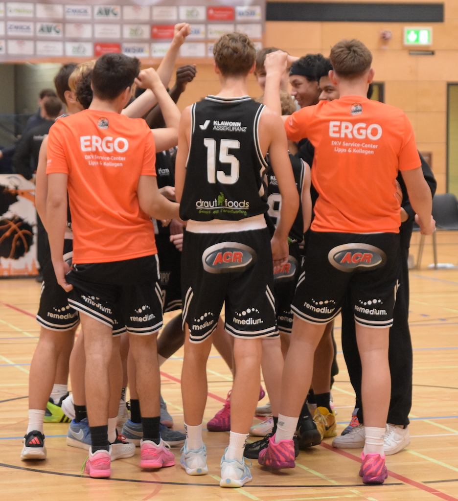 Mehrere junge Basketballspieler in schwarz und orange jubeln gemeinsam im Kreis