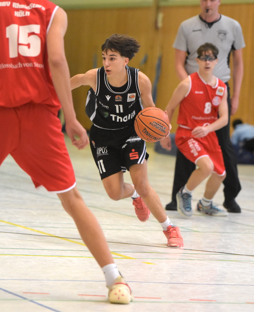 Ein junger Basketballspieler im schwarzen Trikot dribbelt fokussiert den Ball