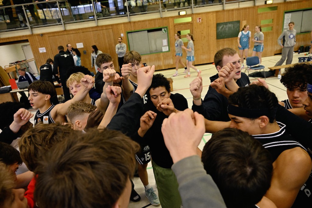 Eine Gruppe junger Basketballspieler mit entschlossenen Gesichtern steht im Kreis und jubelt