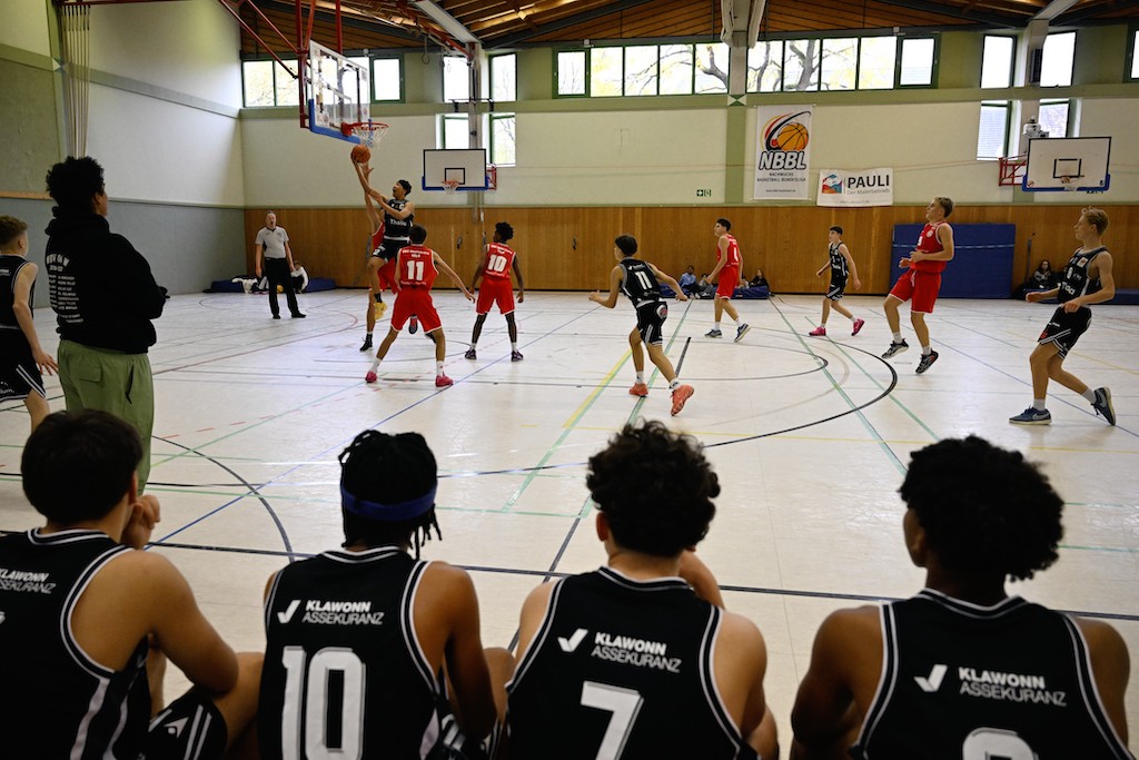Mehrere Basketballspieler in schwarzen und roten Trikots spielen konzentriert in einer Halle