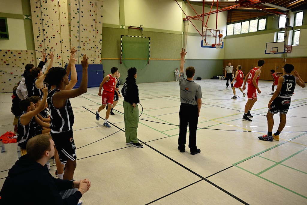 Ein Basketballspieler in Rot wirft einen Freiwurf, andere beobachten gespannt das Spiel
