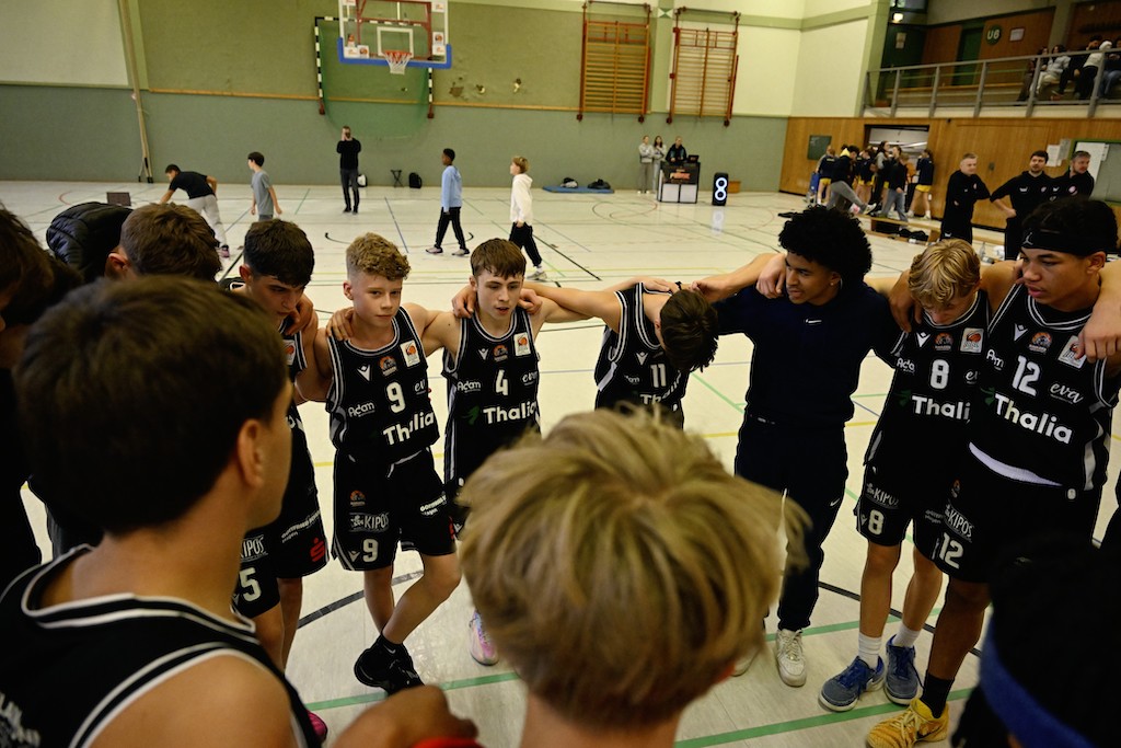 Eine Basketballjugendmannschaft im Kreis in schwarzer Sportkleidung, motiviert und konzentriert