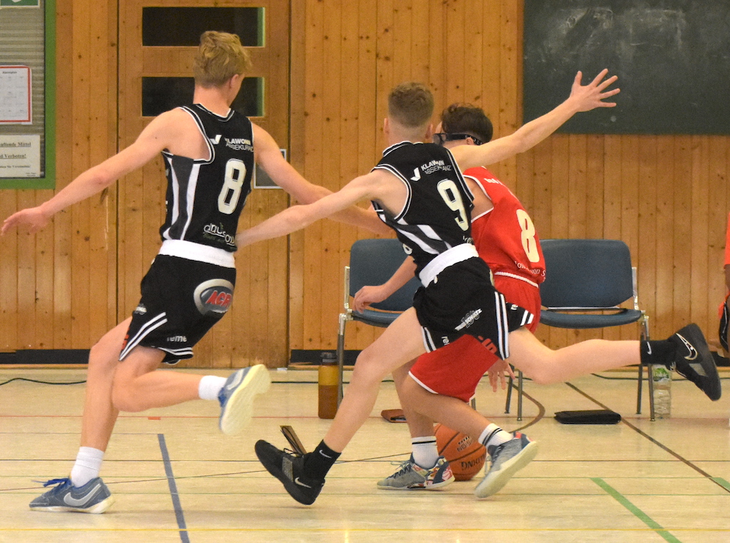 Zwei junge Männer im schwarzweißen Trikot rennen energisch gegen einen roten Spieler
