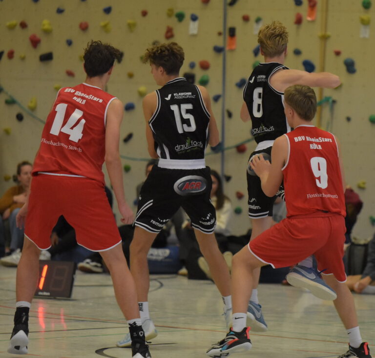 Vier junge Basketballspieler im Spiel auf heller Halle mit bunter Kletterwand im Hintergrund