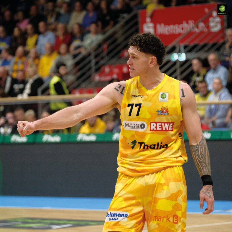 Ein Basketballspieler im gelben Trikot schaut ernst und gestikuliert energisch mit dem Arm