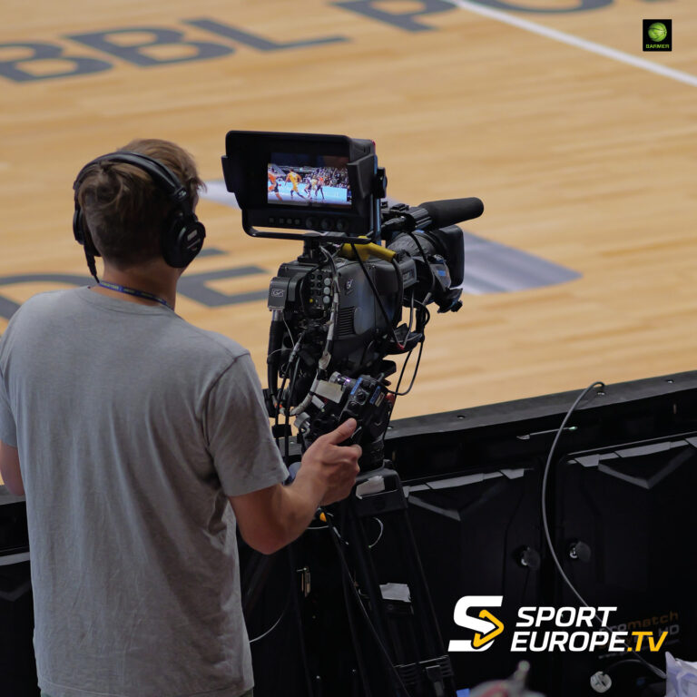 Ein Kameramann filmt ein Basketballspiel in einer Sporthalle.