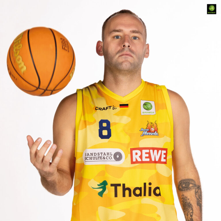 Ein ernster Basketballspieler im gelben Trikot wirft einen Ball in die Luft