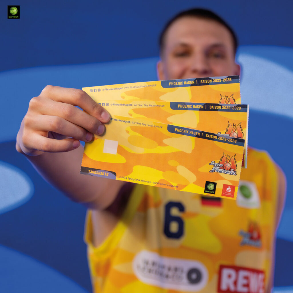 Ein junger Mann im gelben Basketballtrikot hält drei bunte Tickets lächelnd in die Kamera