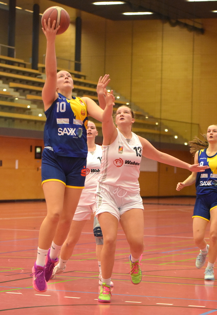 Eine junge Basketballspielerin mit entschlossenem Gesichtsausdruck wirft den Ball zum Korb