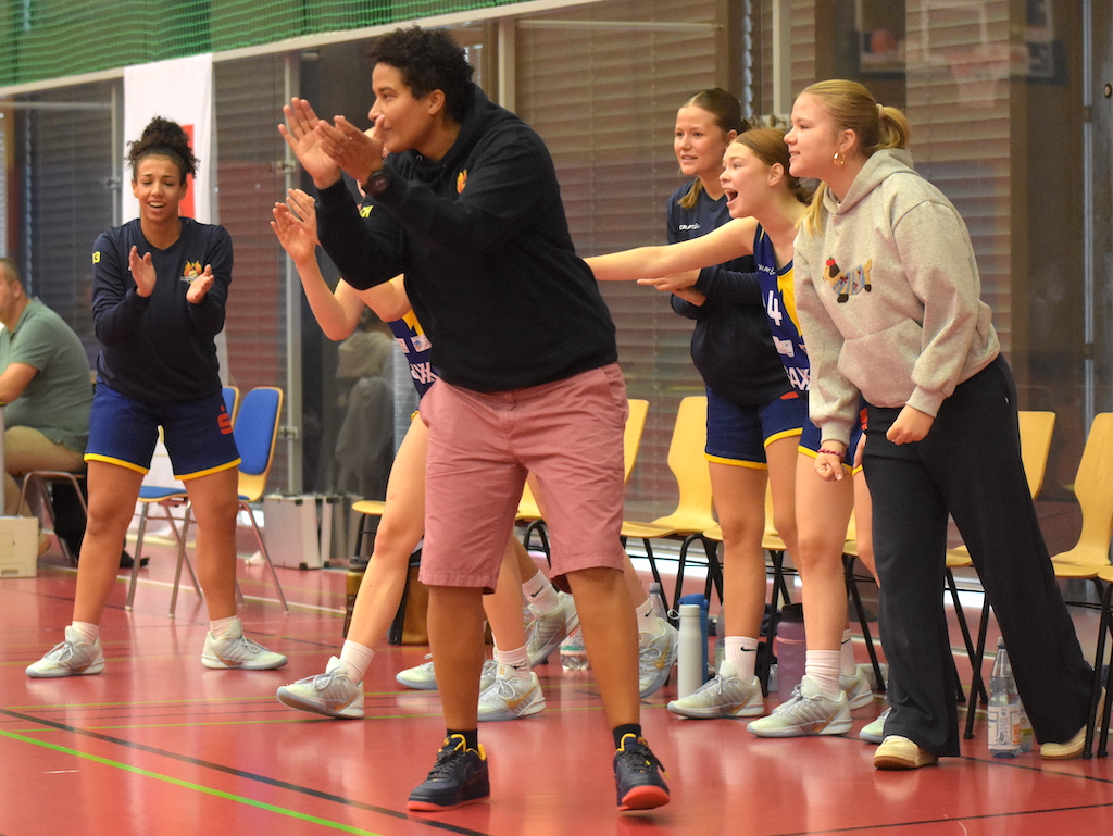Sechs jubelnde Frauen im Sportoutfit und Hoodie feuern begeistert ihr Team an