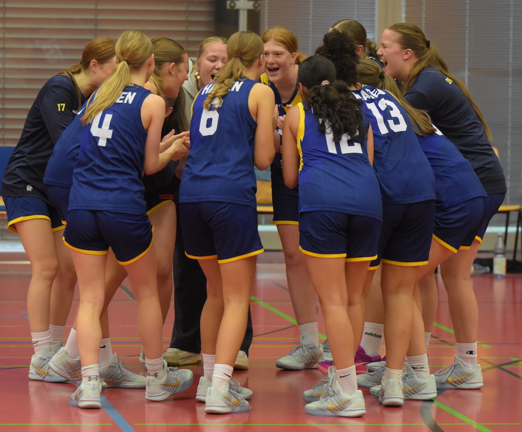 Mehrere Basketballspielerinnen im blauen Trikot lachen und bilden einen Kreis