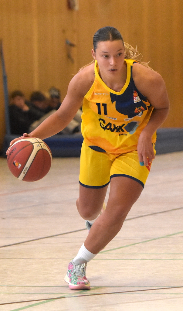 Junge Frau in gelbem Basketballtrikot dribbelt konzentriert einen Ball über das Spielfeld