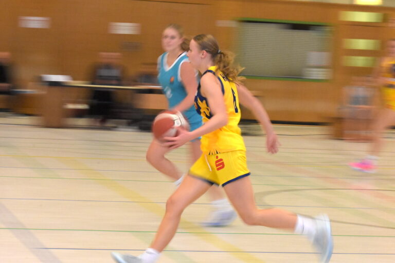 Eine junge Frau im gelben Basketballtrikot läuft konzentriert mit dem Ball übers Spielfeld