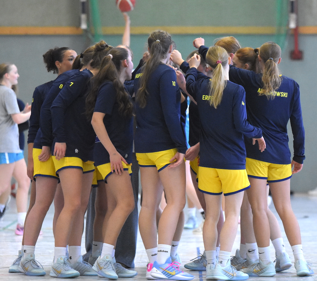 Mehrere junge Frauen im blauen Sportoutfit bilden einen Kreis und strecken die Hände zusammen