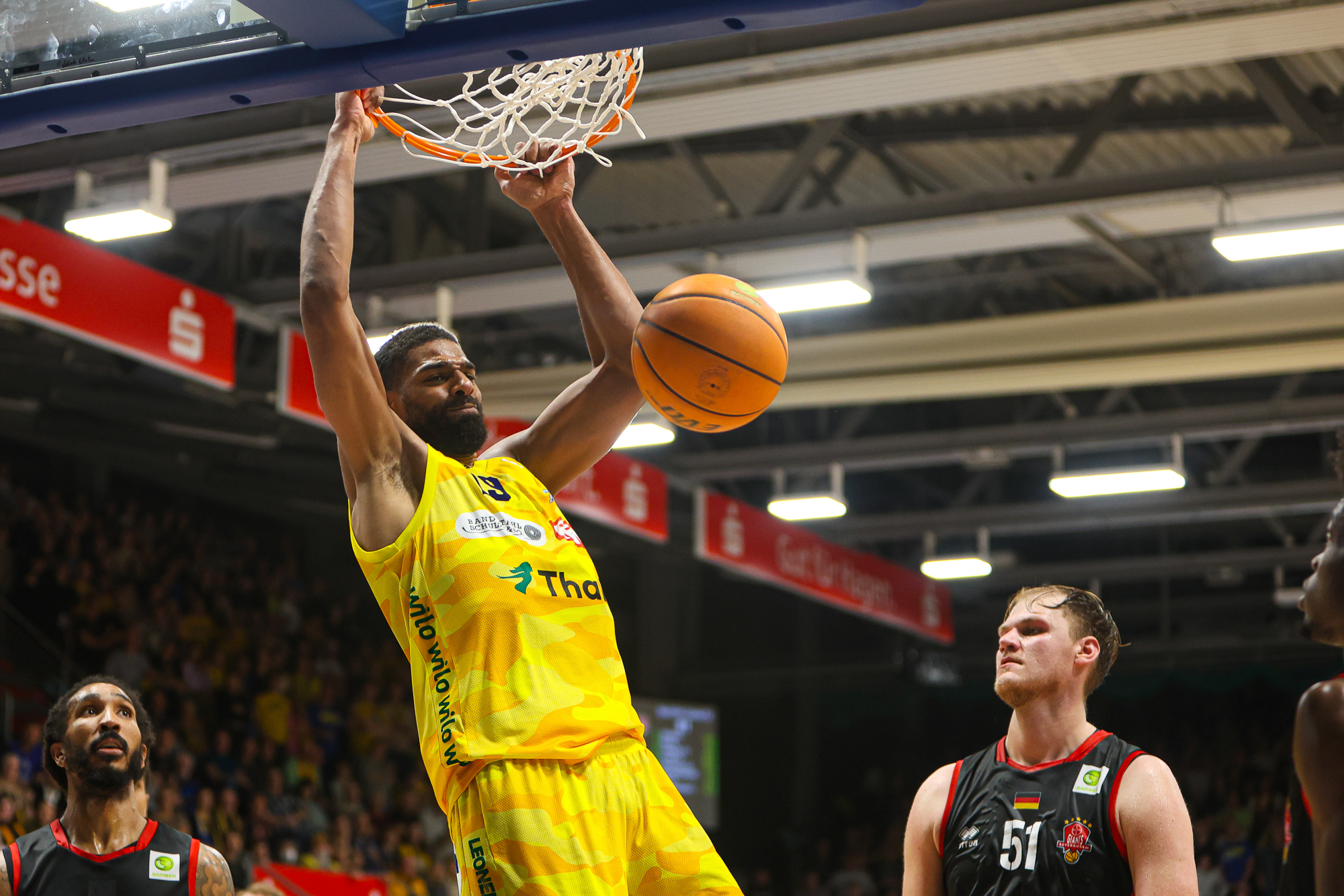 Ein Basketballspieler im gelben Trikot dunkt kraftvoll den Ball durch den Korb