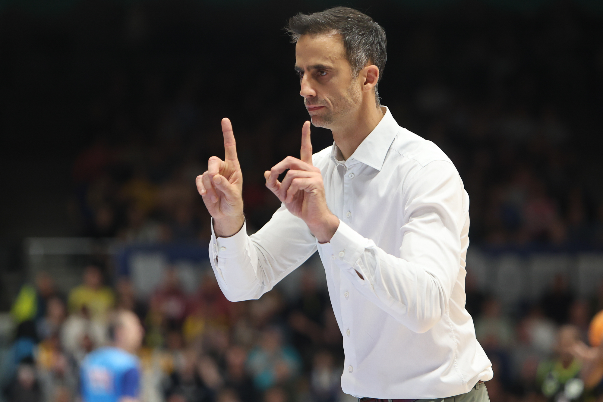 Ein Mann mit ernstem Blick und weißem Hemd gestikuliert mit erhobenen Zeigefingern