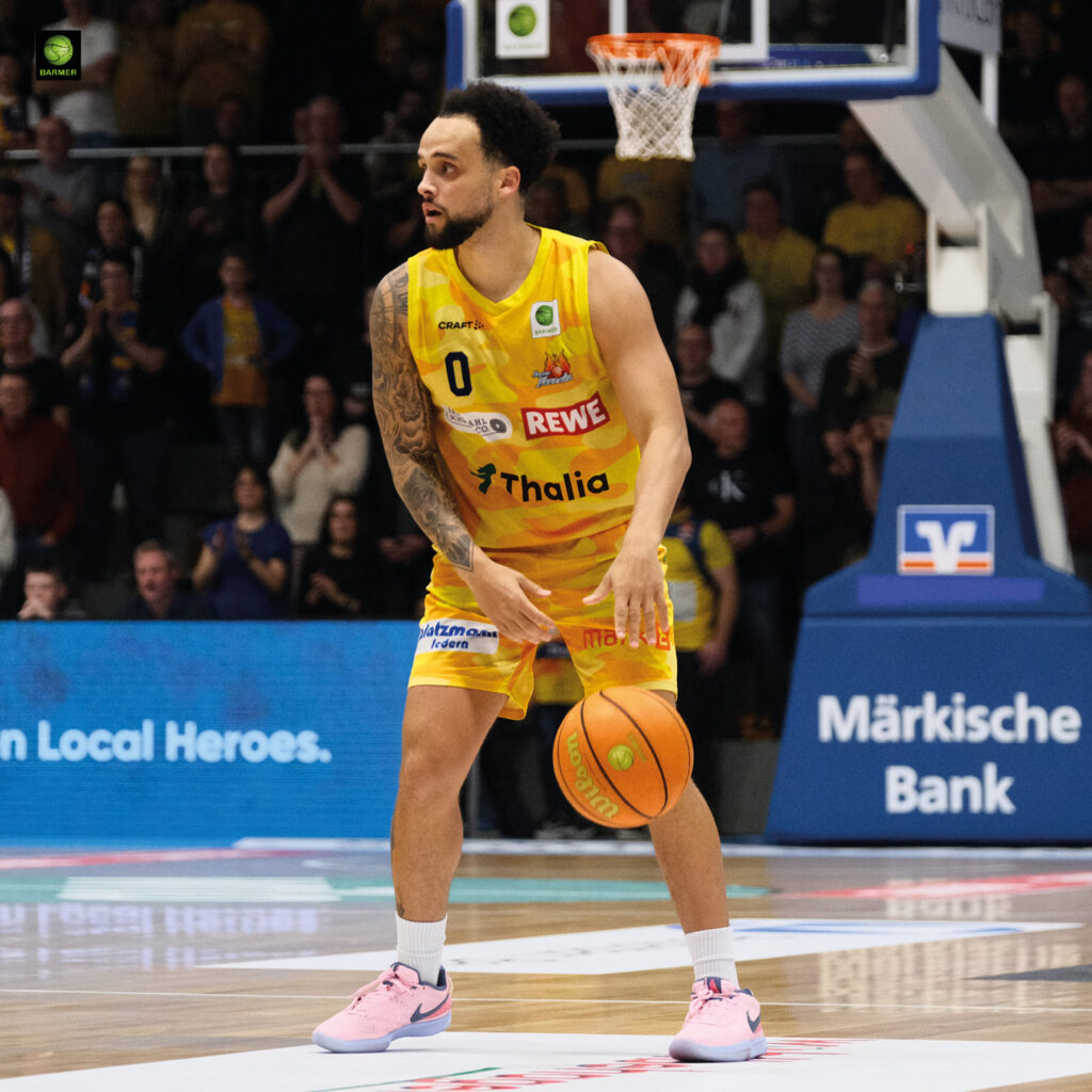 Ein Basketballspieler im gelben Trikot schaut konzentriert und hält den Ball bereit
