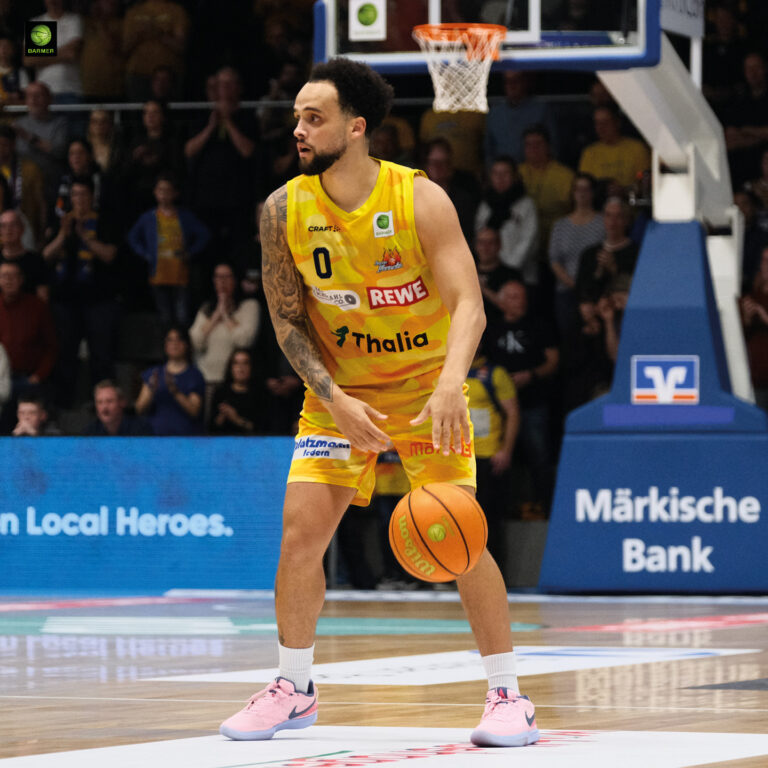 Ein Basketballspieler im gelben Trikot schaut konzentriert und hält den Ball bereit