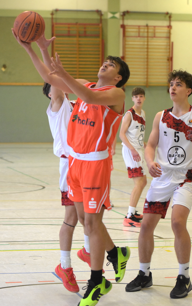 Ein junger Basketballspieler im orangefarbenen Trikot springt konzentriert zum Korb