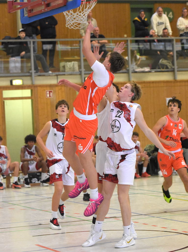 Junger Basketballspieler im orangefarbenen Trikot springt mit entschlossenem Blick zum Korb