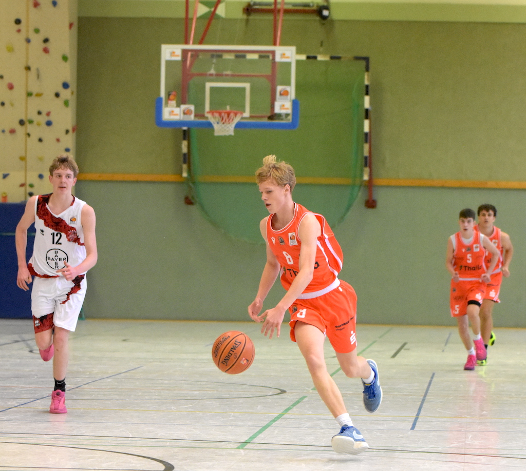 Ein junger Mann im orangefarbenen Basketballtrikot dribbelt konzentriert den Ball
