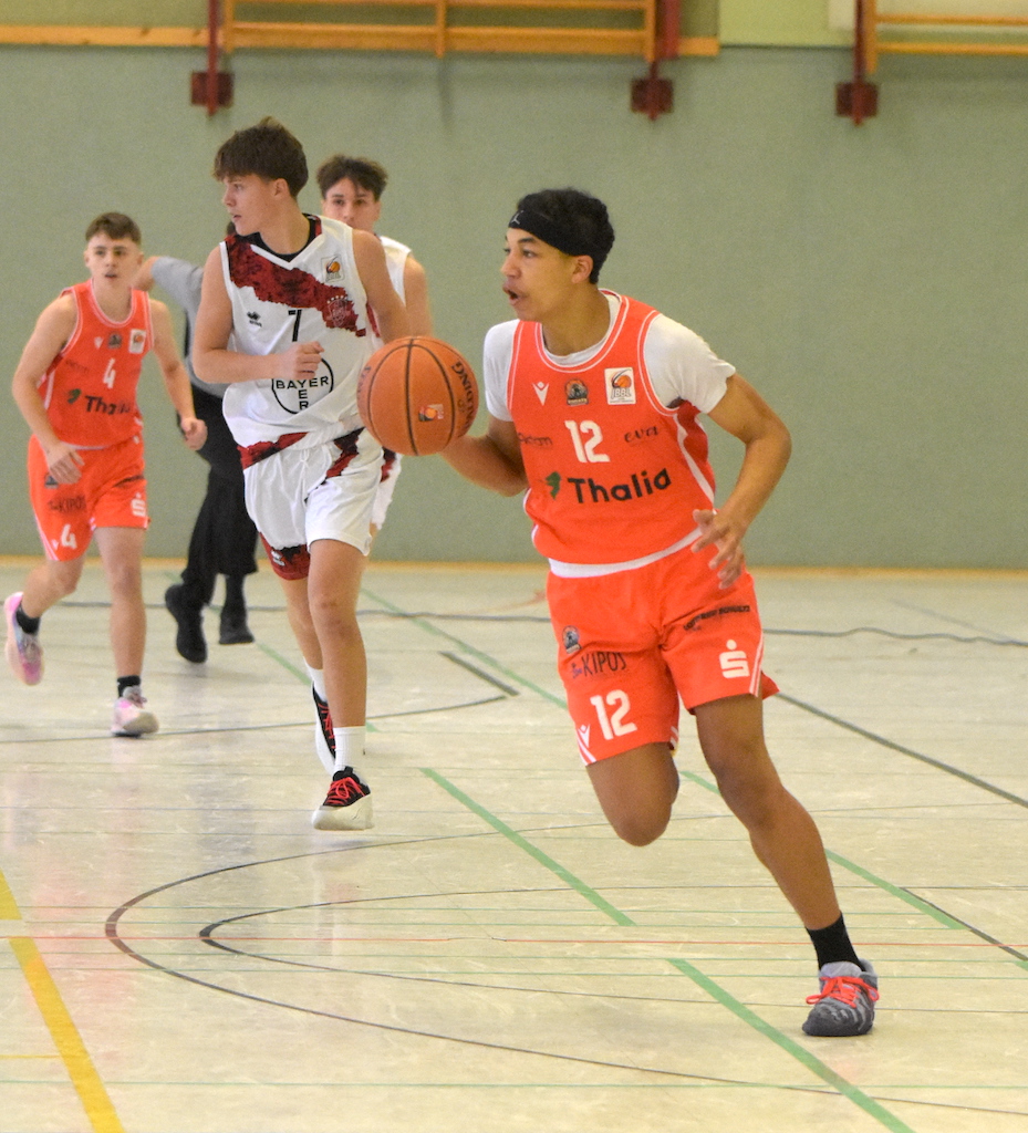 Ein junger Basketballspieler im orangen Trikot dribbelt konzentriert den Ball vorne