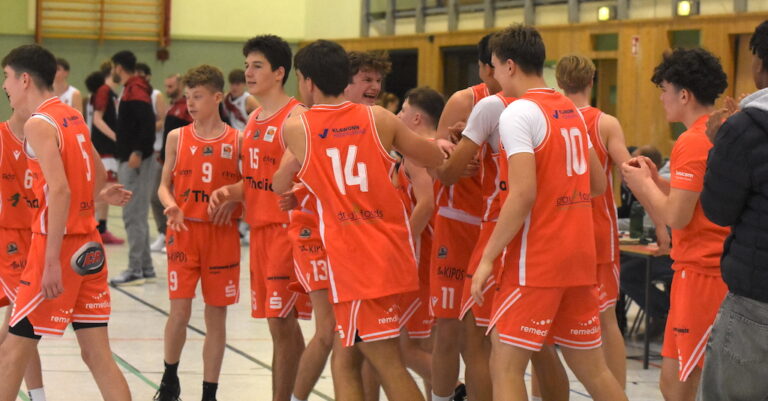 Mehrere junge männliche Basketballspieler im orangefarbenen Trikot freuen sich jubelnd