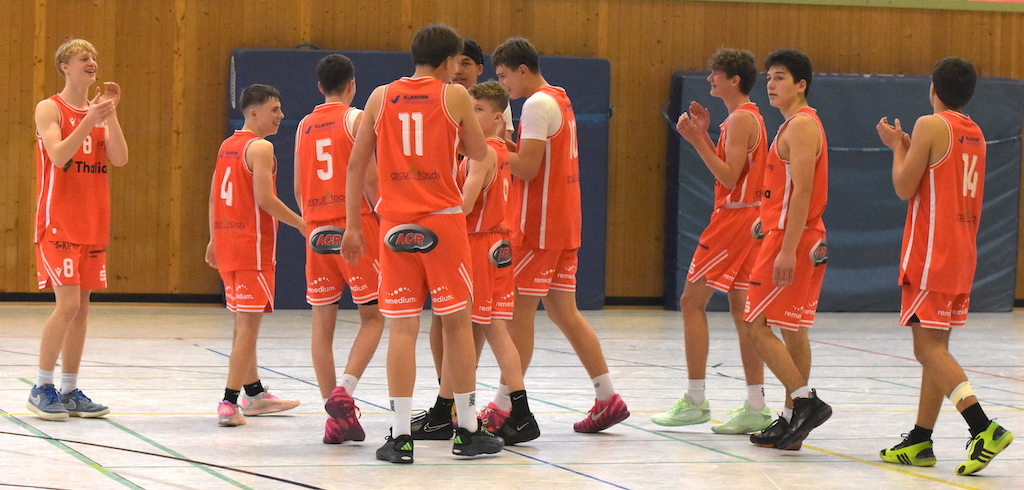 Mehrere jugendliche Basketballspieler im orangefarbenen Trikot jubeln lachend zusammen