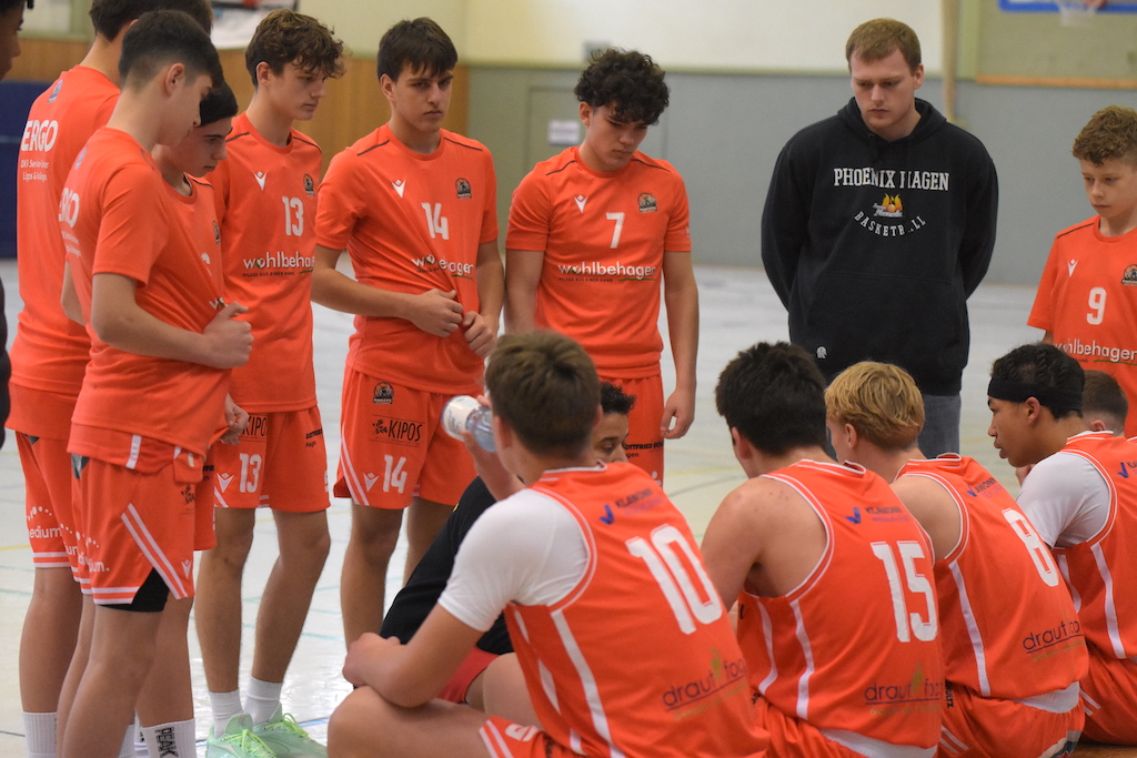 Eine Basketballmannschaft in orangefarbenen Trikots lauscht aufmerksam ihrem Trainer