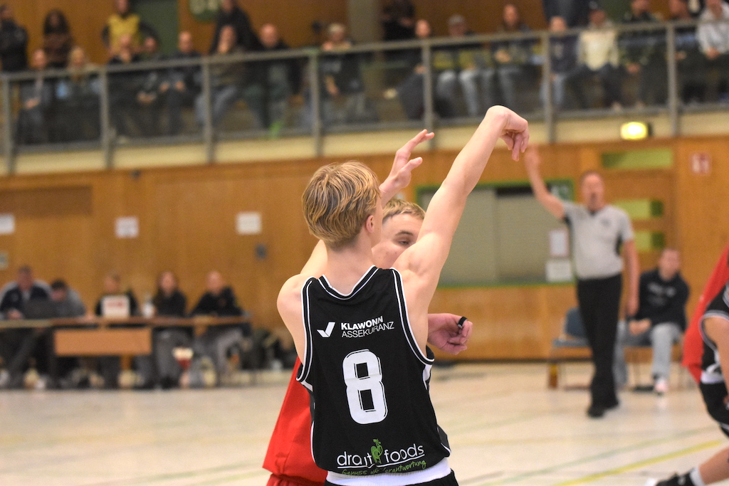 Jugendlicher mit blondem Haar wirft konzentriert einen Basketball in einer Sporthalle