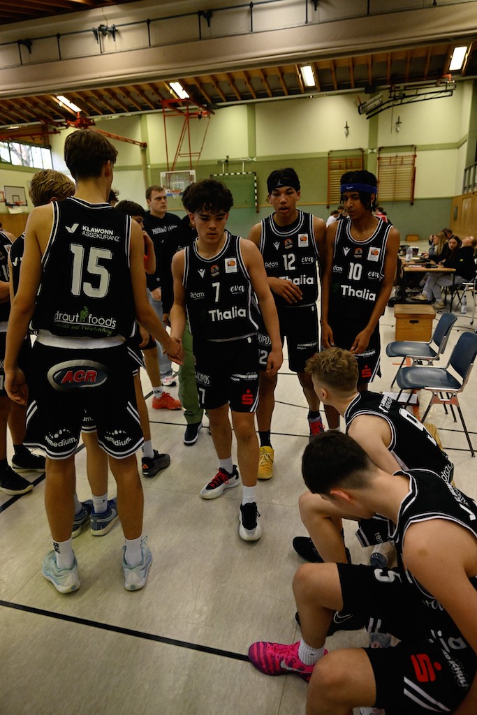 Mehrere jugendliche Basketballspieler in schwarzen Trikots besprechen sich konzentriert