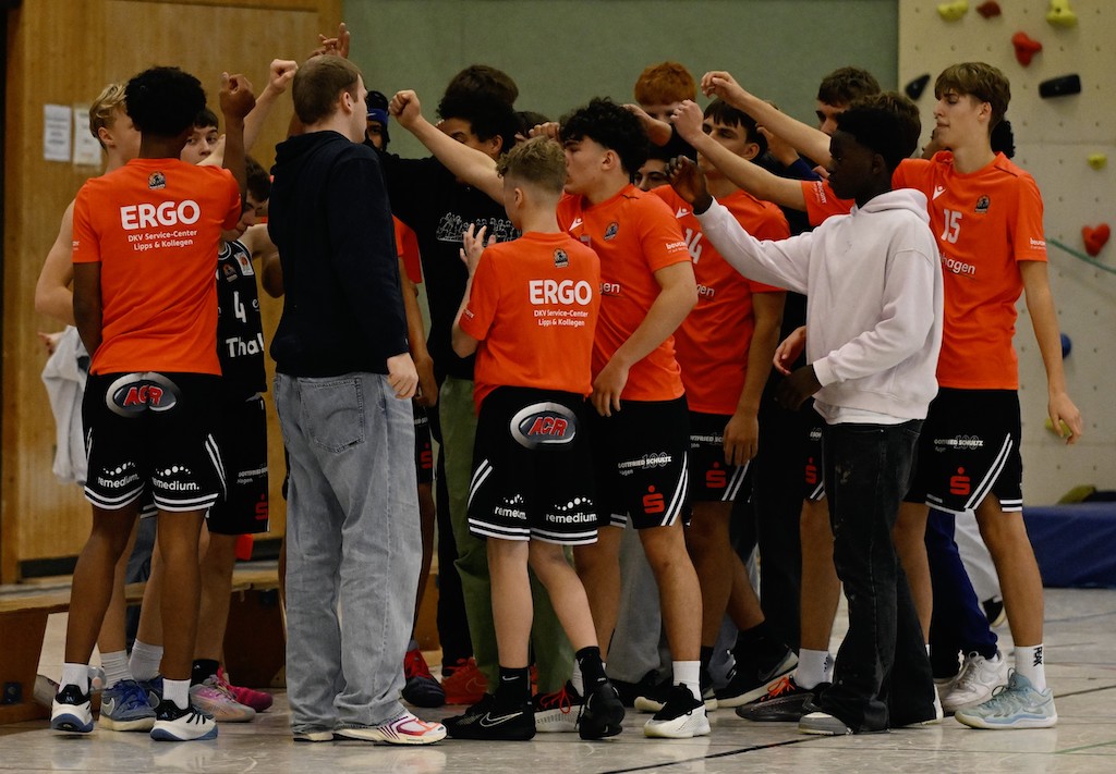 Eine männliche Jugendmannschaft mit orangen Trikots steht motiviert im Kreis zusammen